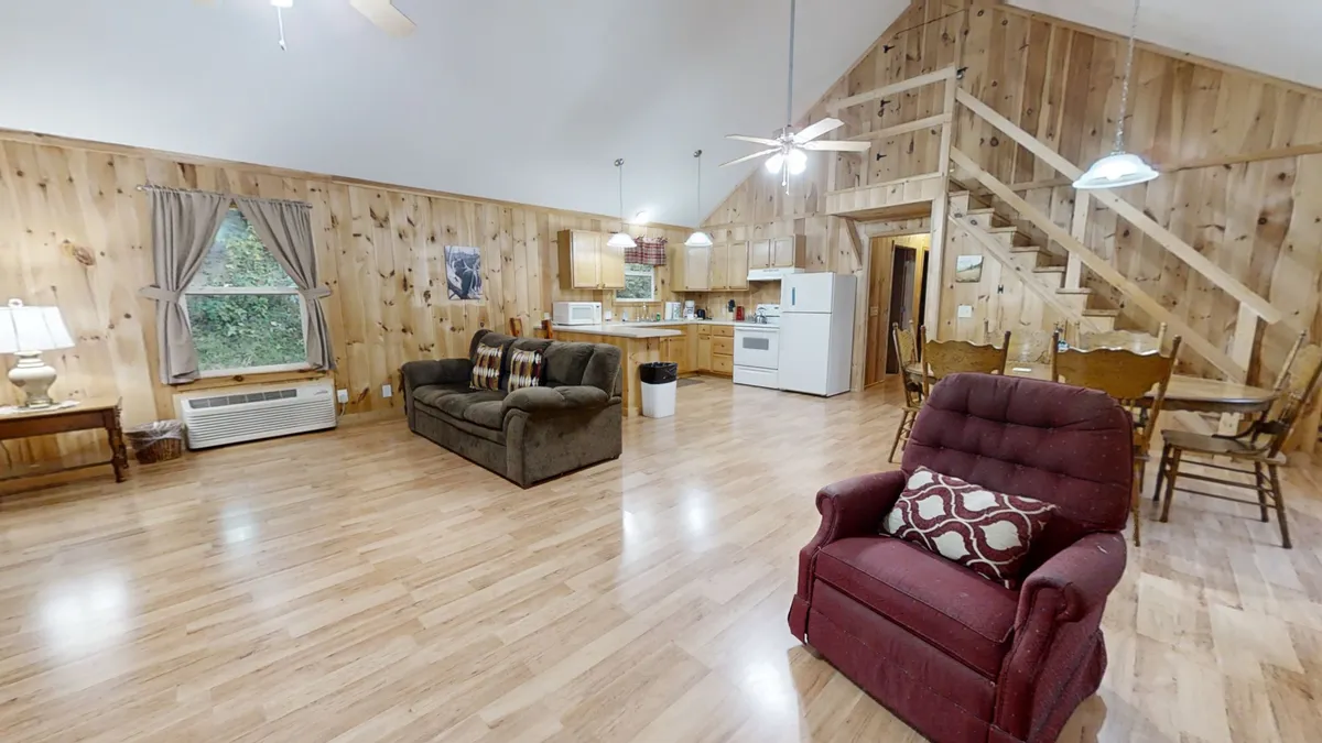 This image displays a broader view of the open interior, featuring the sofa, recliner, dining table, and a glimpse of the adjoining kitchen area. The arrangement is ideal for family gatherings, game nights, and seamless movement between spaces, reinforcing the room's suitability for multiple activities.