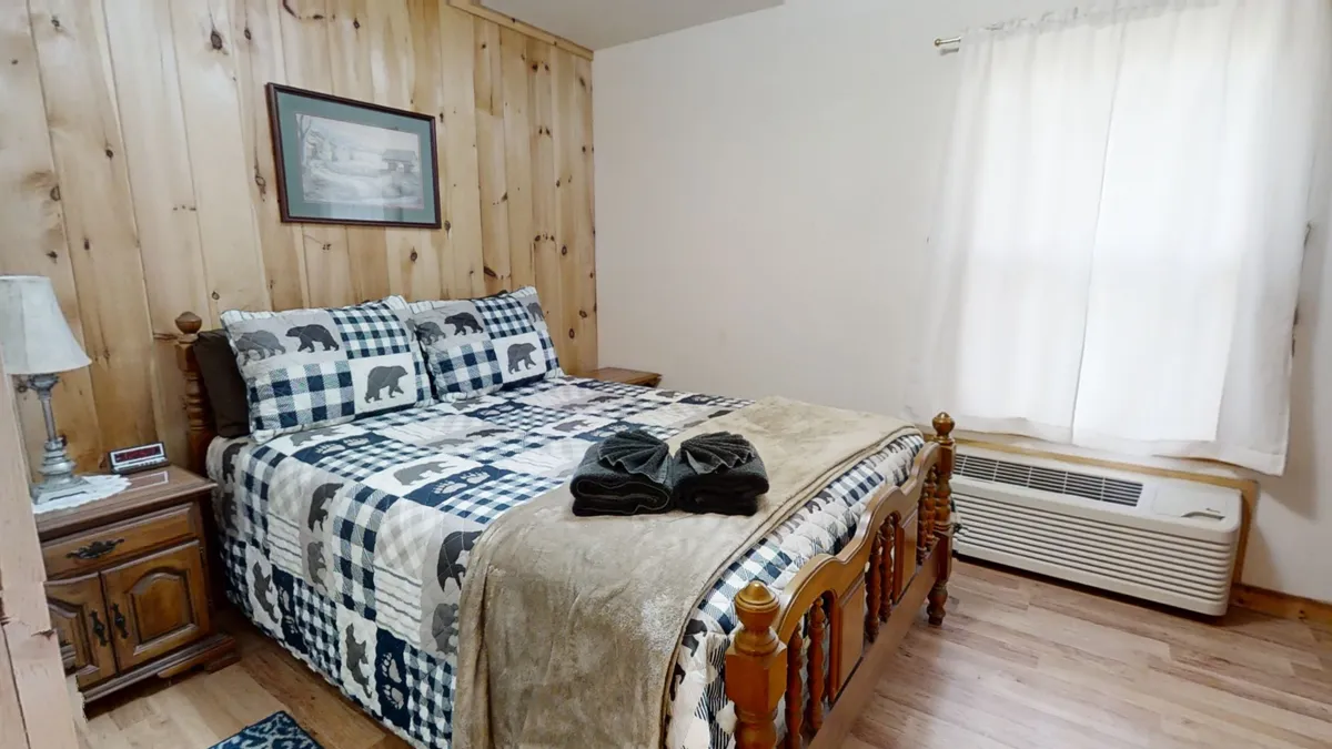 This image showcases a queen bed adorned with patterned bedding, set against warm wooden paneling. A framed picture hangs on the wall, and soft natural light filters into the space, creating a comforting and restful atmosphere ideal for relaxation.