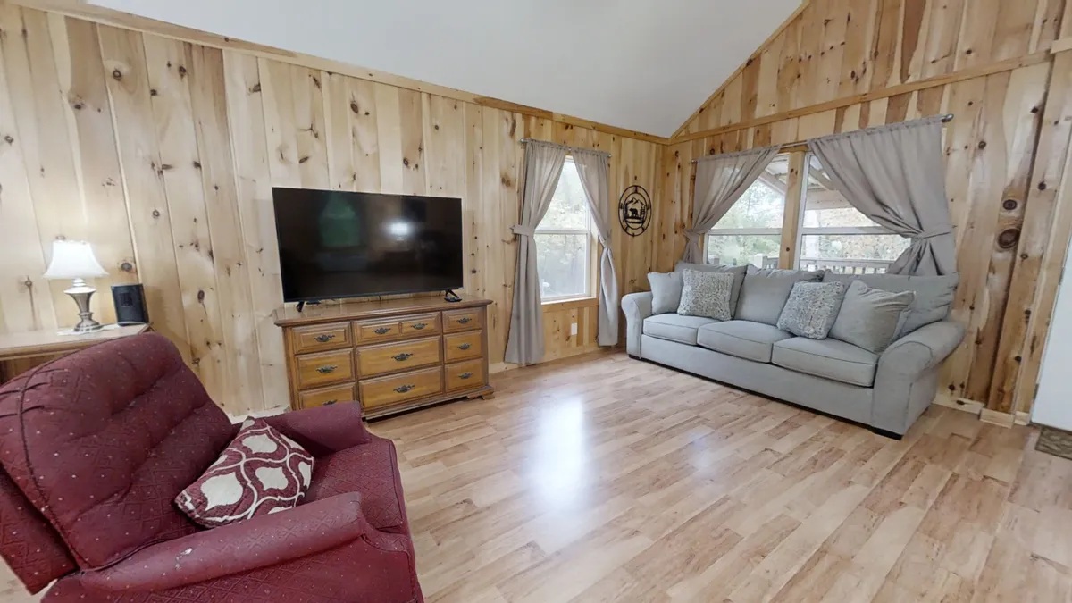 This image showcases a comfortable living room with a sofa, television, wood paneling, and a window with curtains. The room exudes a homey atmosphere, perfect for relaxing, watching TV, or socializing with family and friends. The wood paneling adds a touch of historic charm while the furnishings create a cozy, inviting space.